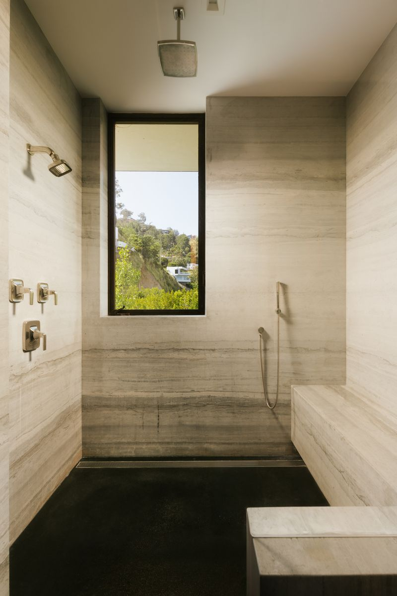 To the left is a spacious walk-in shower wrapped in full-height stone slabs with a built-in bench.