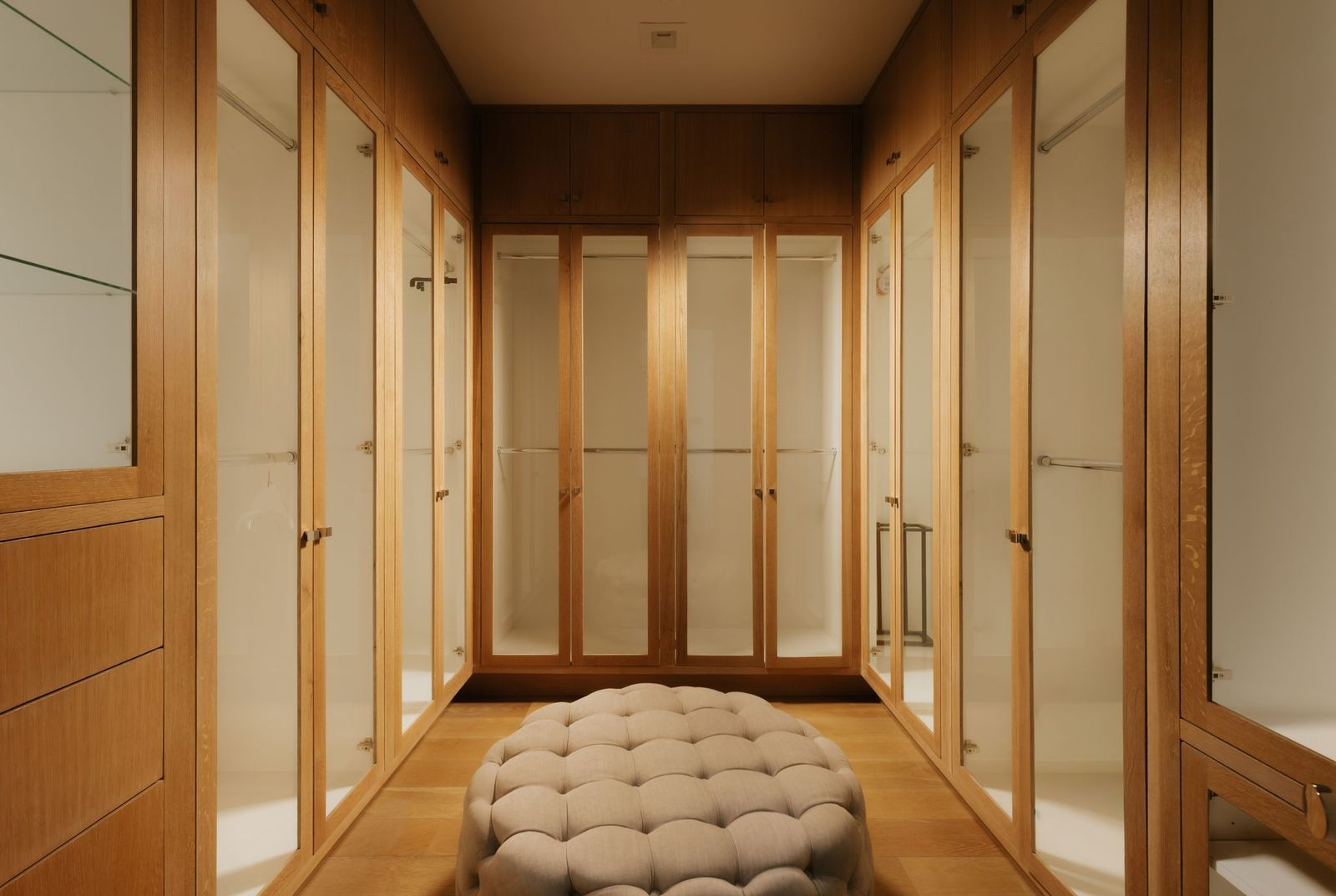 Walk-in closet lined with custom wood cabinetry, illuminated glass-front wardrobes, and built-in drawers.