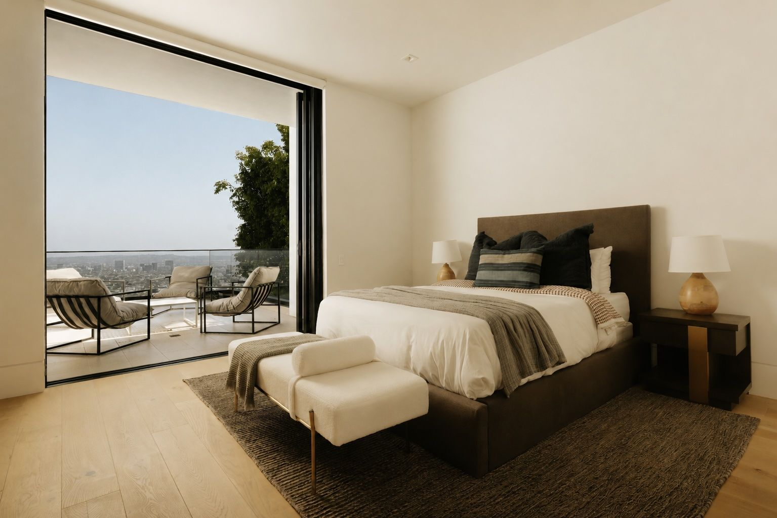 The bedroom includes a bed, matching side tables, and a bench at the foot of the bed that opens directly onto a private terrace through retractable glass doors. 