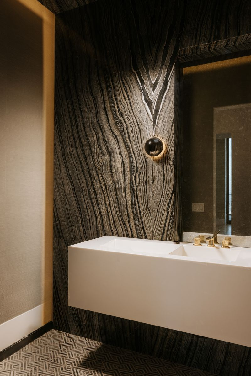 Its en-suite bathroom features a floating white sink set against a dramatic slab of heavily veined natural stone, paired with contemporary fixtures and geometric floor tile.