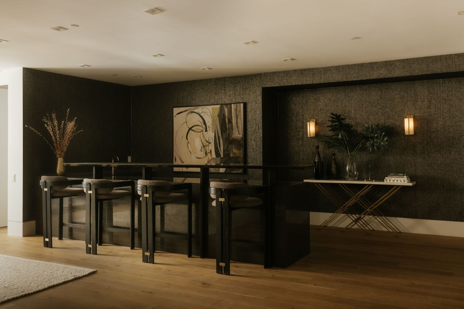 Behind the couch, a sleek black bar stretches across one wall with seating for several guests, creating a natural gathering space for drinks before or after a game or movie.