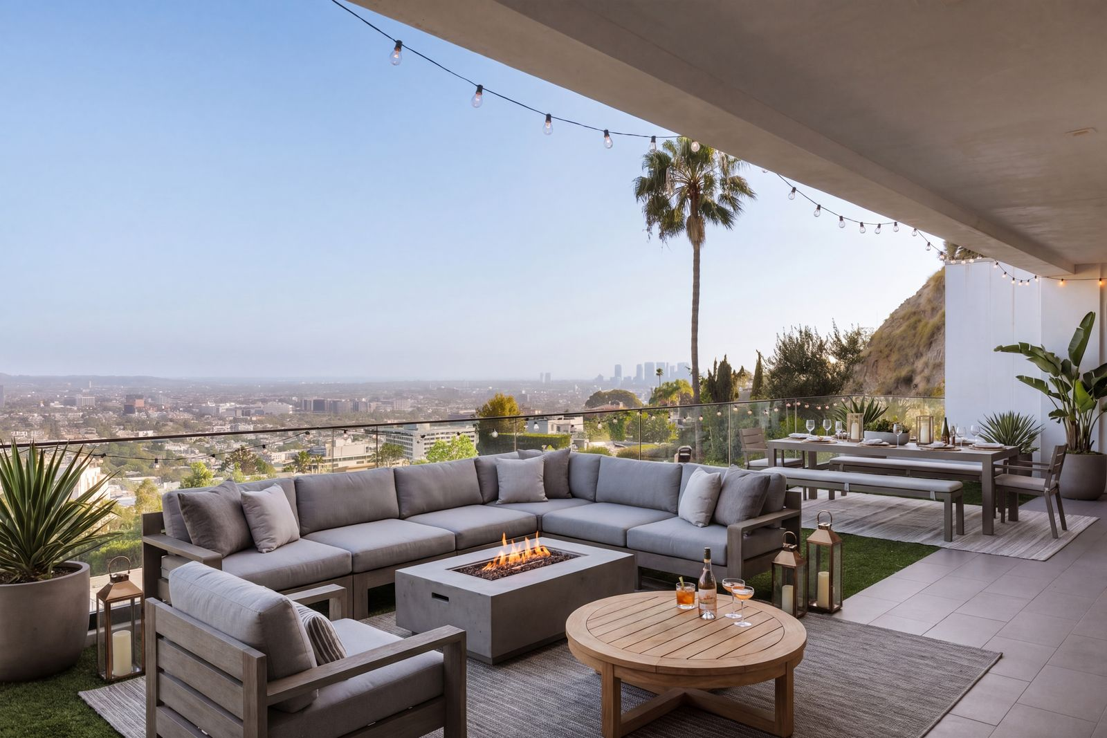 A large sectional surrounds a linear fire pit overlooking the city, while an outdoor dining area accommodates open-air meals beneath string lighting.