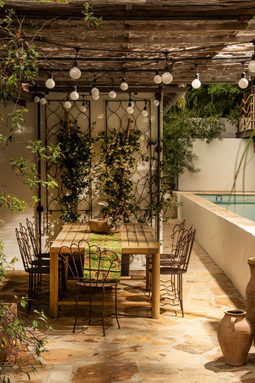 String lights are woven throughout the overhead structure, while climbing jasmine and surrounding plants soften the stone patio, creating the perfect setting for casual meals and gatherings.
