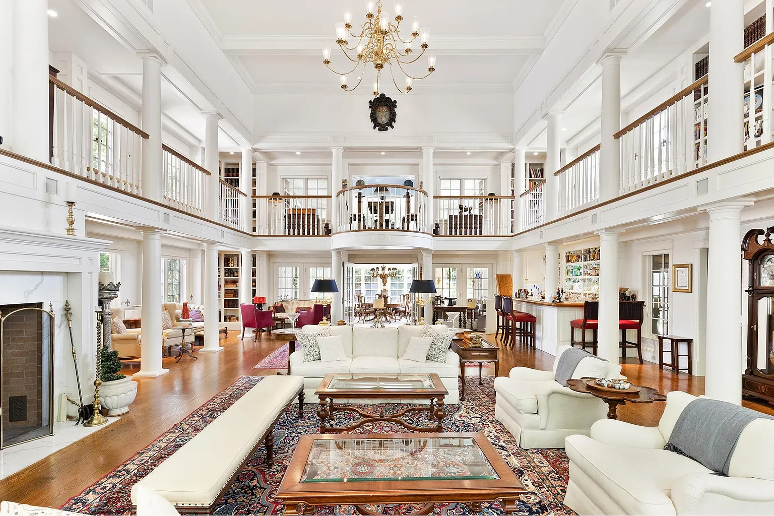 The heart of the main house is a dramatic two-story great room framed by soaring ceilings, white millwork, and a symmetrical arrangement of columns that support wraparound second-floor galleries.
