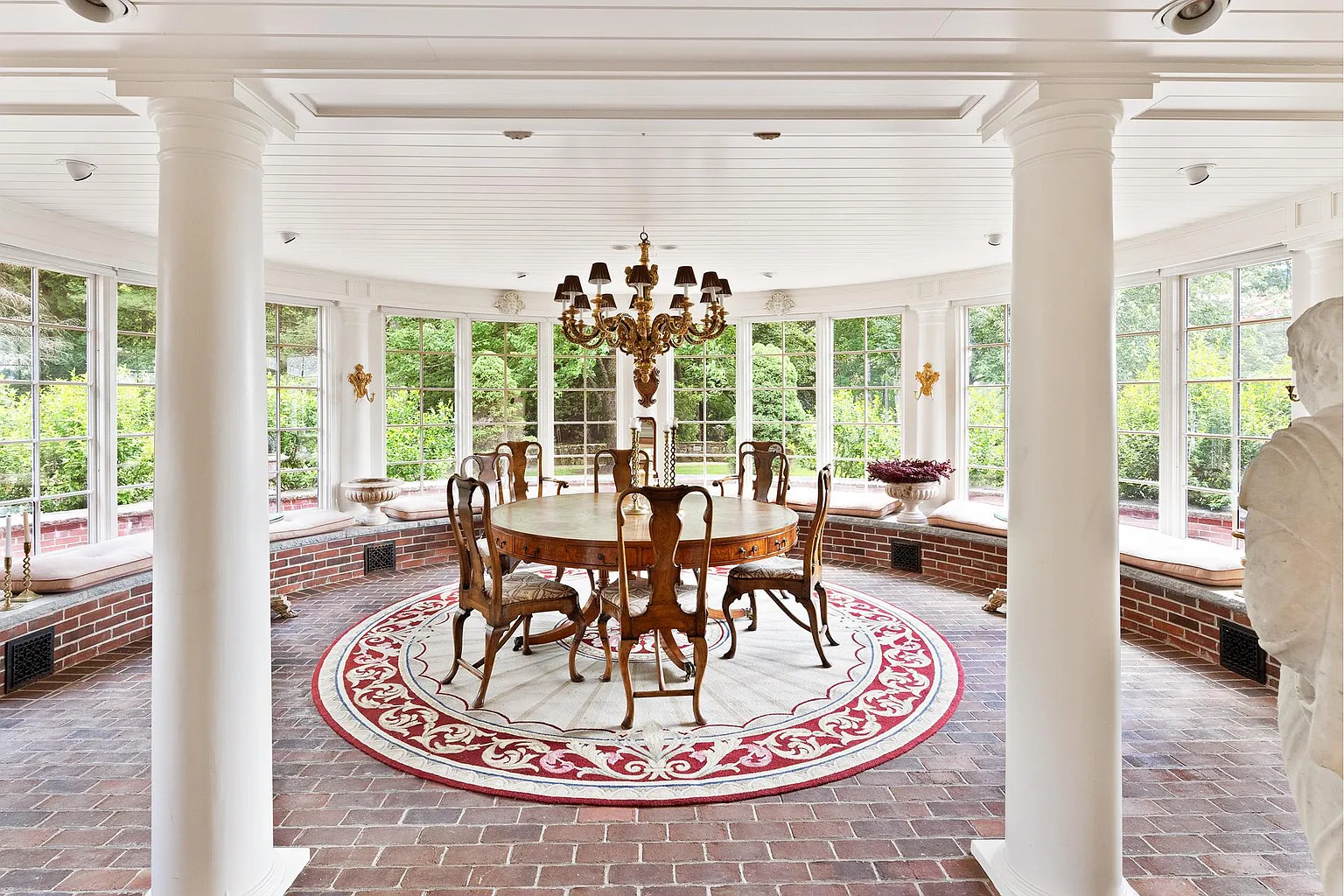 A circular dining table sits beneath a chandelier at the center of the room, while built-in brick window benches wrap around the perimeter.