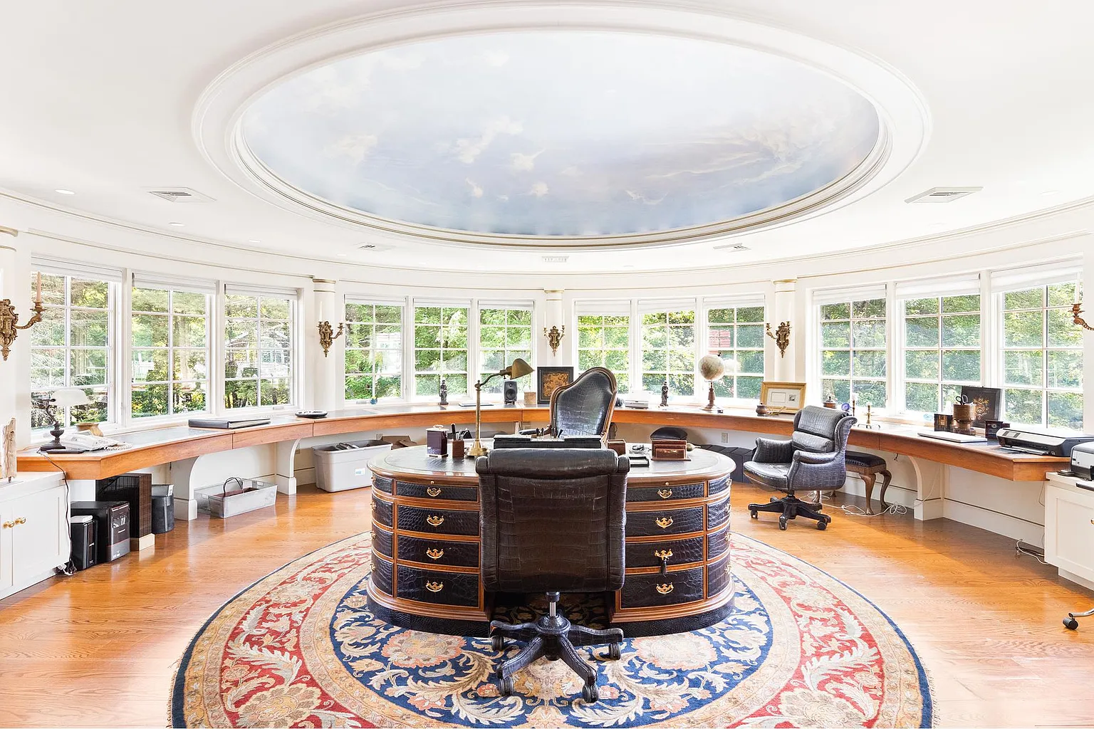 The home office is designed as a circular executive workspace, with a custom round desk positioned beneath a painted domed ceiling that depicts a blue sky with drifting clouds. 