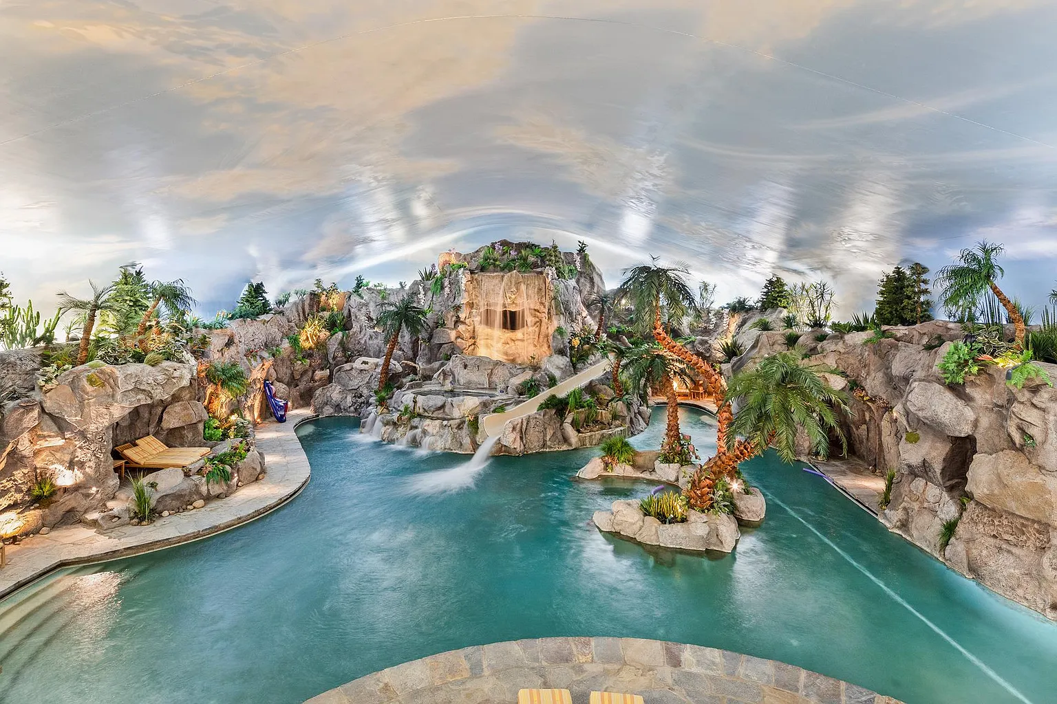 Private indoor water park, centered around a lagoon-style pool surrounded by rock formations, waterfalls, tropical landscaping, and winding pathways. 