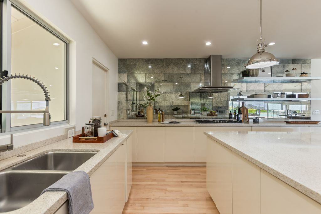 Glossy custom cabinetry lines the perimeter, paired with open shelving and a textured stone tile backsplash.