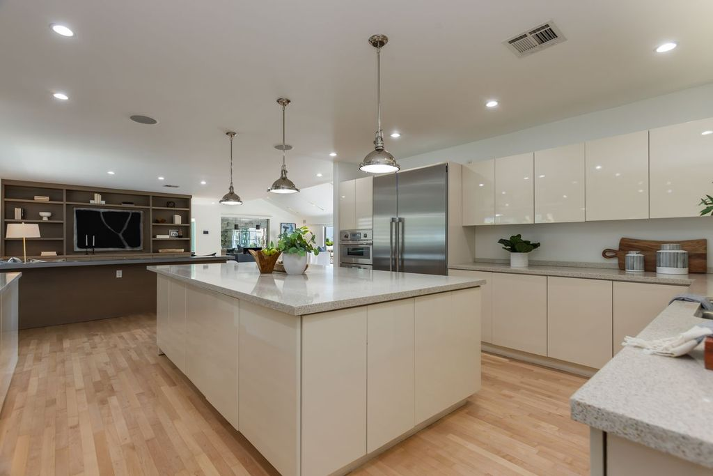 A full suite of Thermador appliances, including built-in ovens, a gas cooktop, oversized refrigerator, and additional prep sink, completes the space. 