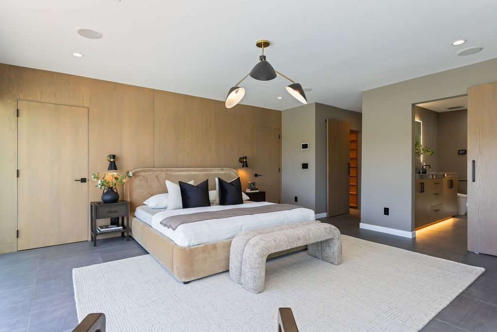 The bedroom features a warm, minimalist design centered around a wood-paneled accent wall and wide-plank flooring. 
