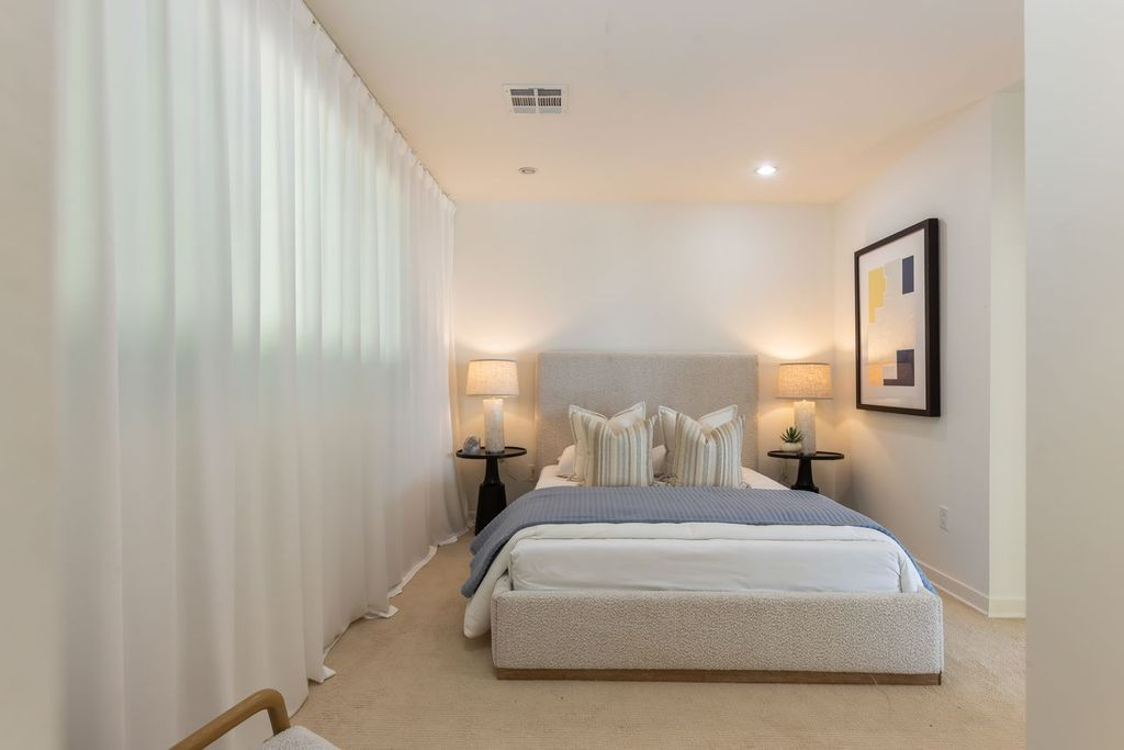 Floor-to-ceiling sheer drapery stretching along one wall and a low-profile upholstered bed framed by matching bedside tables.