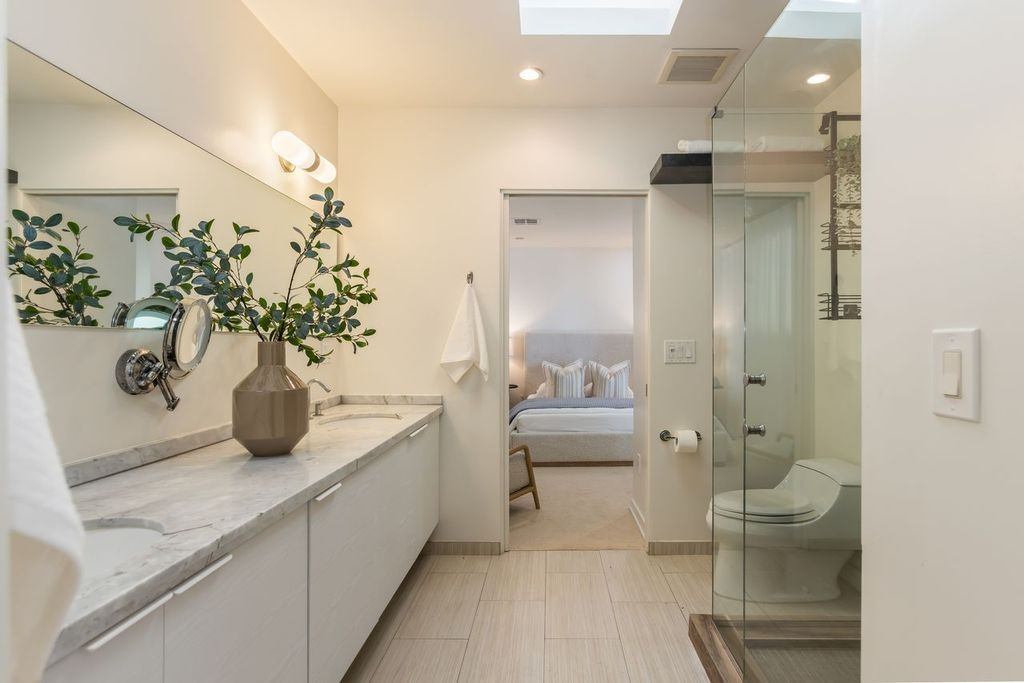 This suite's bathroom mirrors the home's modern aesthetic with a floating marble vanity, glass-enclosed shower, and overhead skylight.