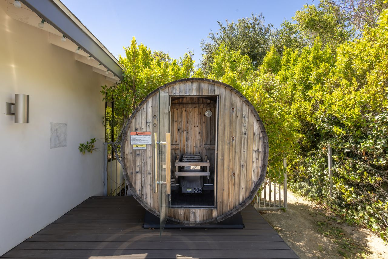 Tucked around the corner of the home, a cedar barrel sauna adds a private wellness feature to the backyard surrounded by lush greenery.