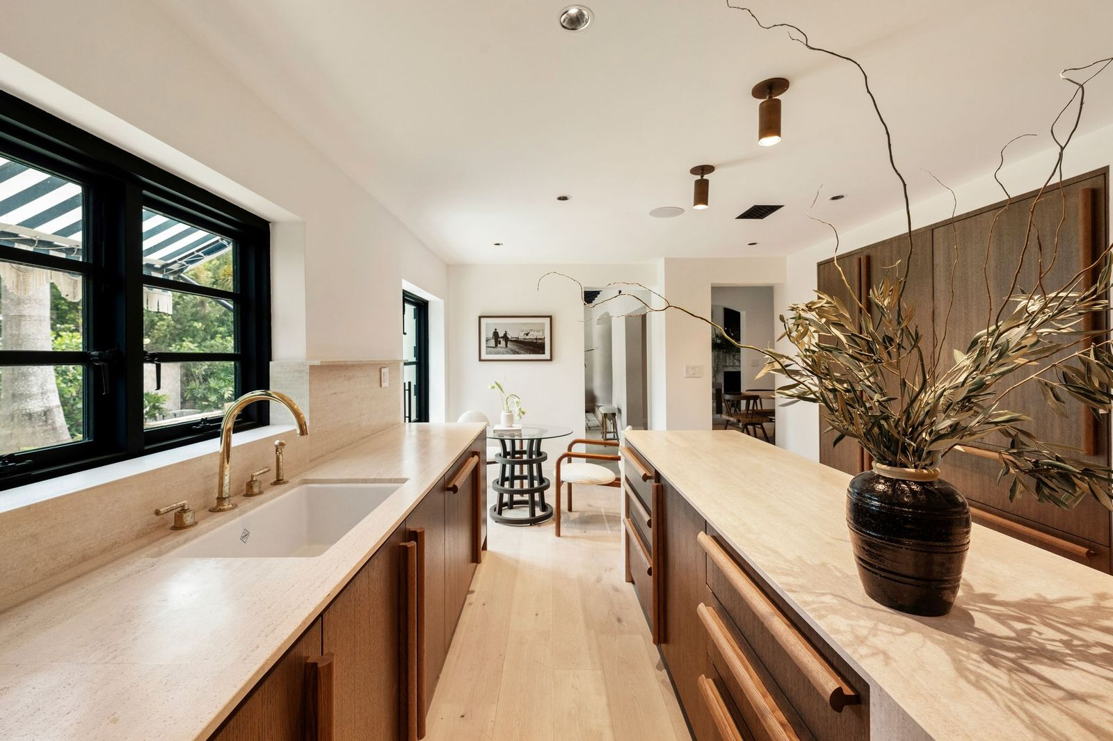 Bespoke white oak cabinetry wraps the perimeter, complemented by matching integrated panels and a neutral stone backsplash that extends beneath the windows. 
