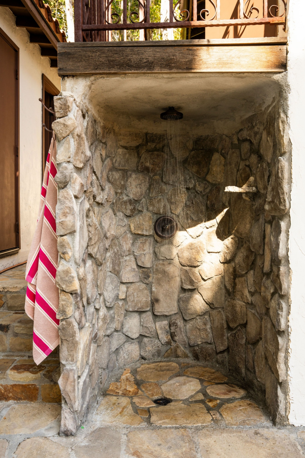 Tucked beneath an elevated deck, a stone shower offers a convenient place to rinse off after a swim. 