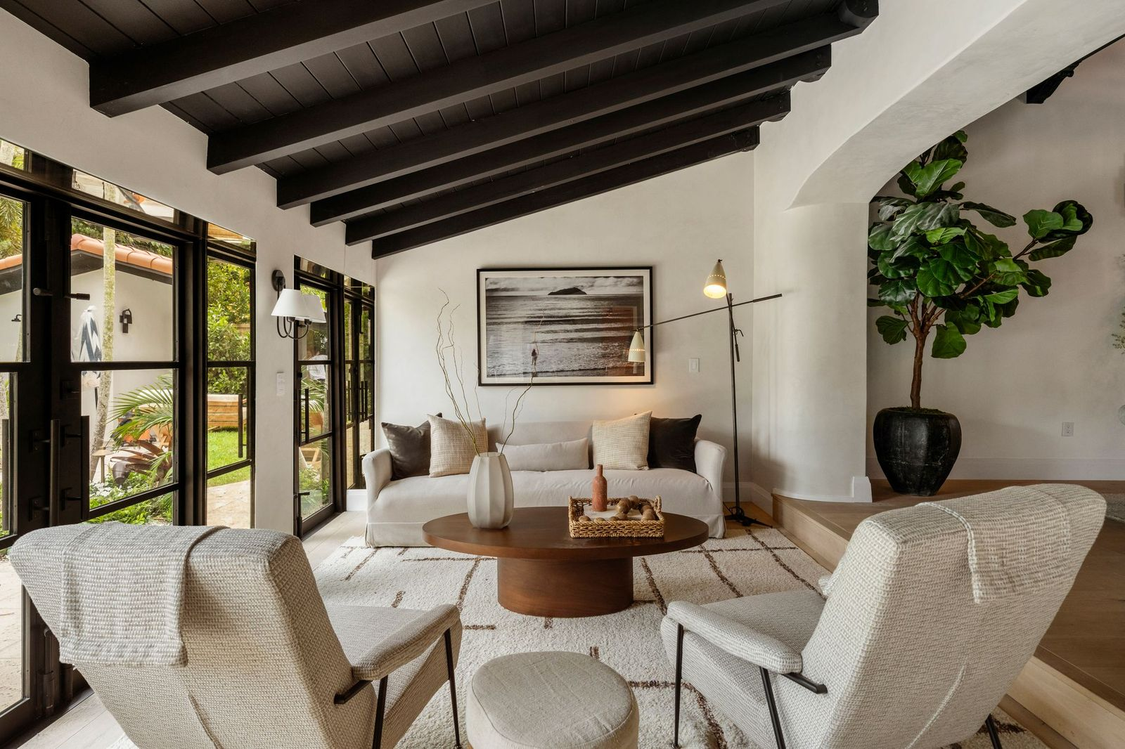Dark exposed ceiling beams line the ceiling, while oversized custom black-framed windows and French doors line the exterior wall. 