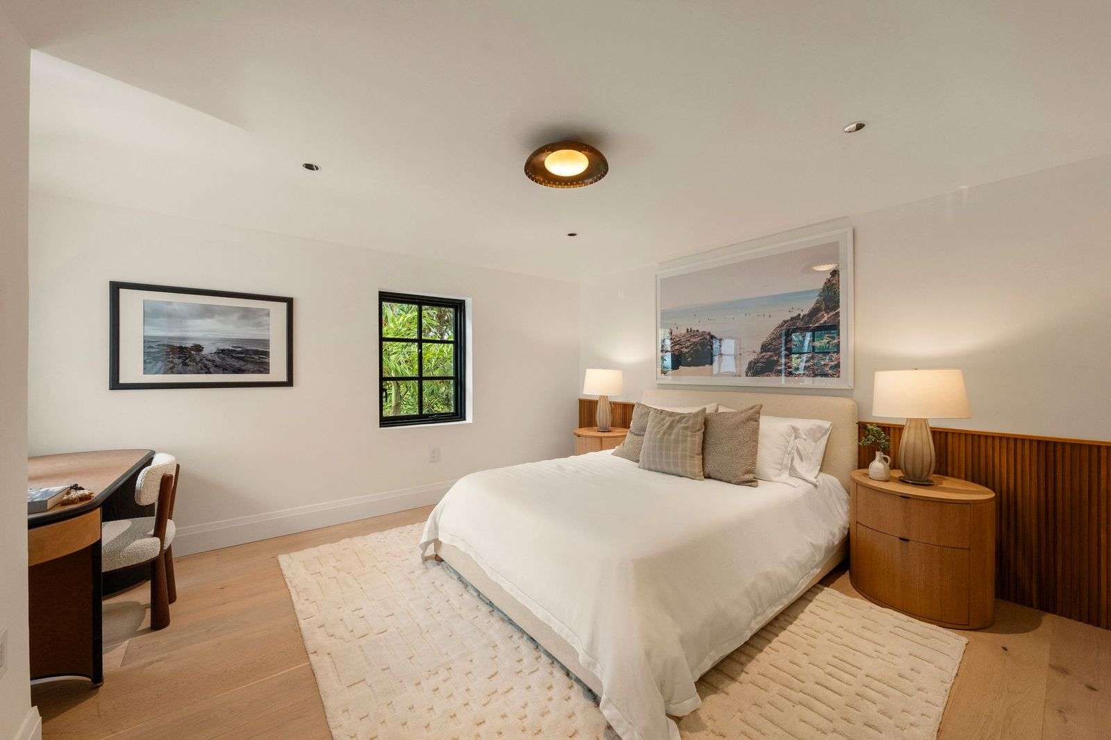 The first bedroom features wide-plank wood flooring, crisp white walls, and a bed framed by fluted wood wainscoting that continues behind matching nightstands. 