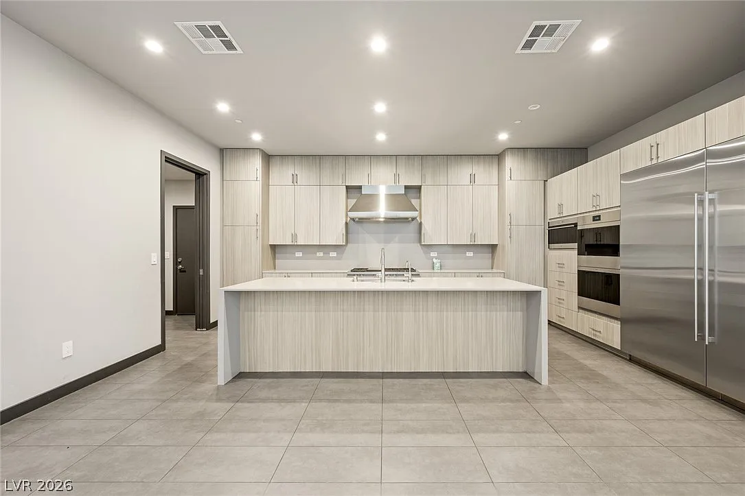 A large waterfall-edge island provides seating and additional prep space, while custom floor-to-ceiling cabinetry wraps the perimeter to maximize storage.