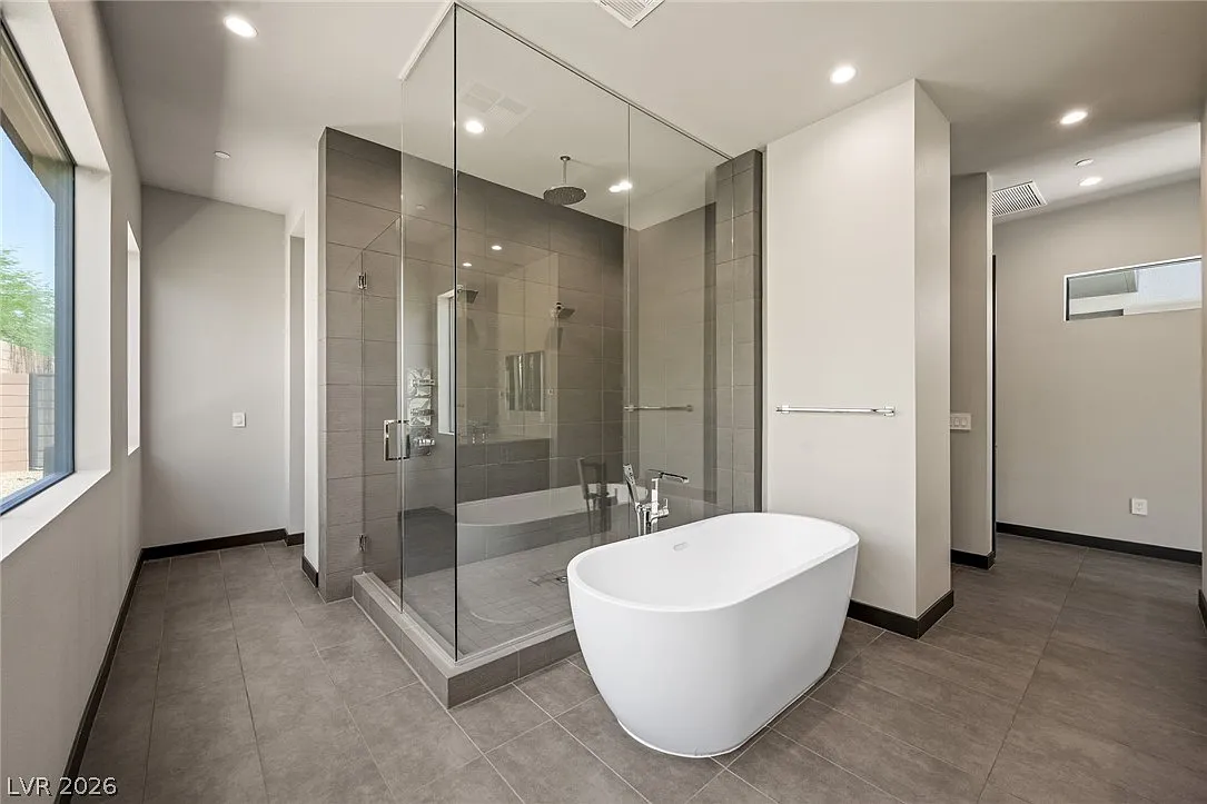 White free standing soaking tub sits in front of a glass-enclosed walk-in shower.