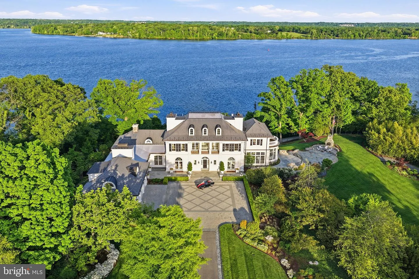 The white exterior rises above a broad paved courtyard, with symmetrical windows, French doors, and a slate roof reinforcing the home's classic design.