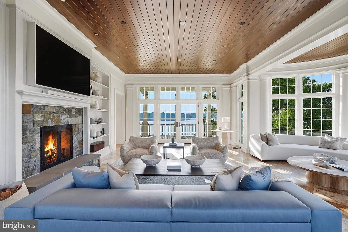 To the left, a stone fireplace creates the center of the room, surrounded by blue and white couches made to complement the river views.