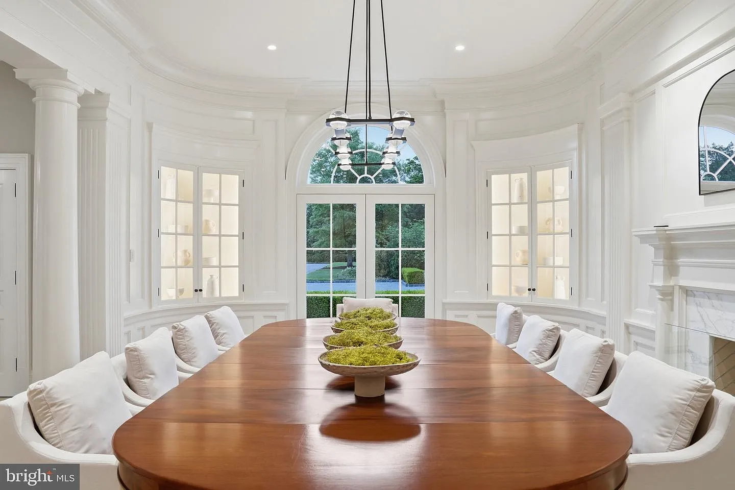 Fluted columns, detailed millwork, and a sweeping circular ceiling create a sense of symmetry, while a large arched window and French doors bring natural light into the space.