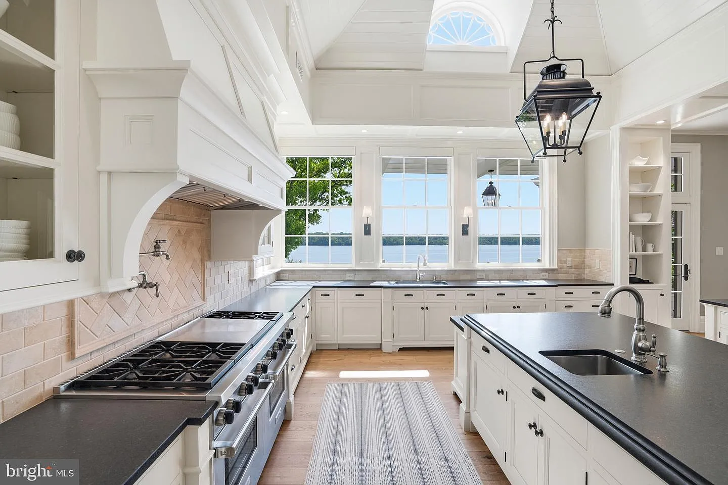 The sink is positioned directly beneath river-facing windows, while built-in shelving, professional-grade appliances, and direct access to the terrace allow the kitchen to flow naturally into the surrounding living spaces.