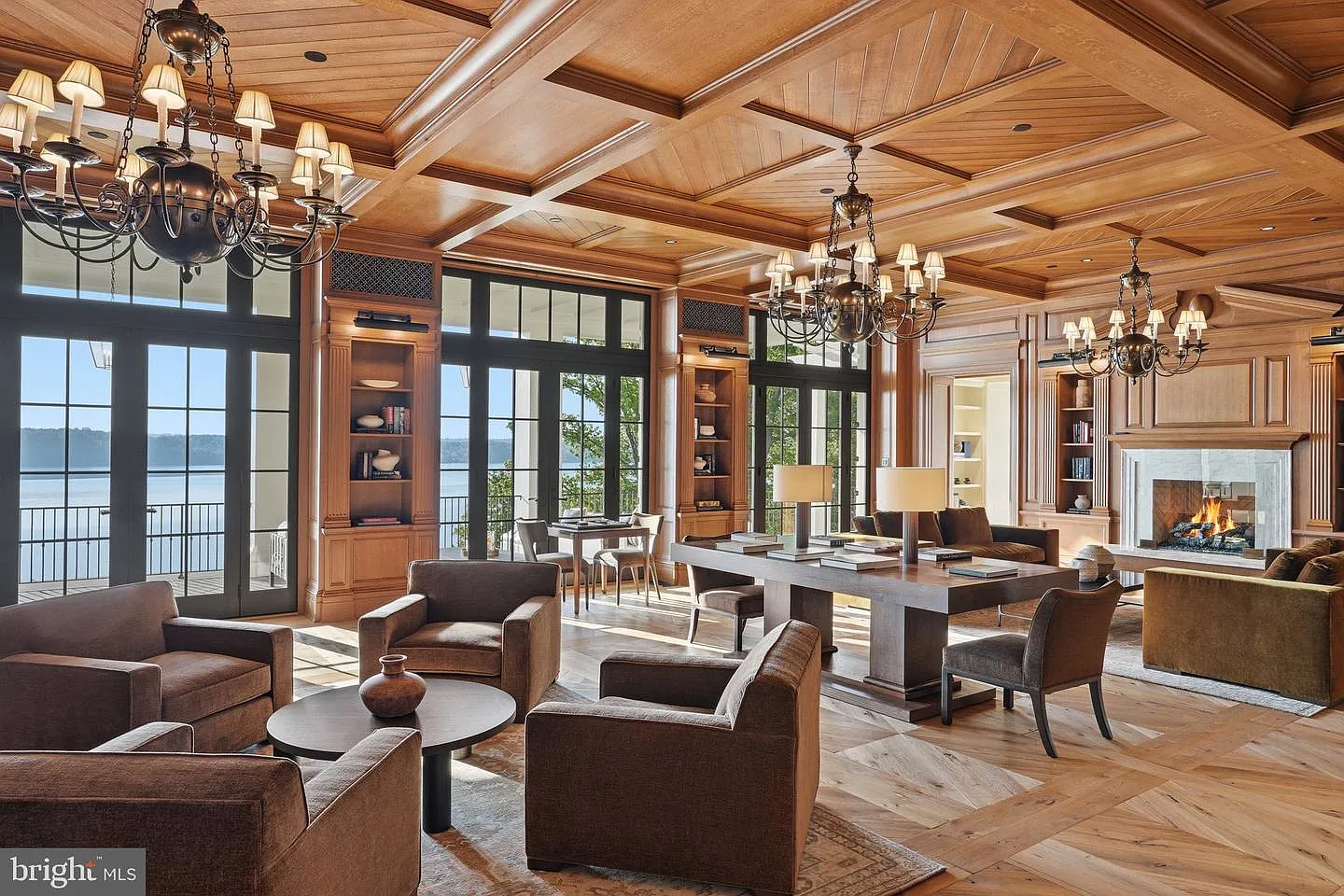 Rich wood paneling wraps the walls from floor to ceiling, while multiple chandeliers hang above several seating areas and a fireplace.