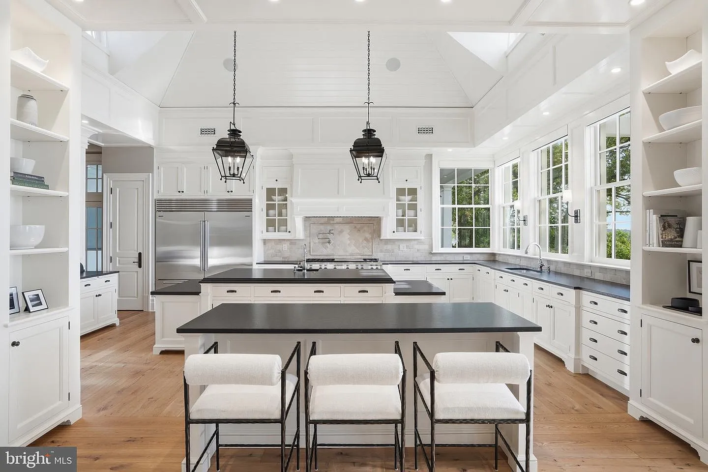 White custom cabinetry wraps the perimeter, complemented by dark countertops and a large central island that serves as both a prep space and casual gathering spot. 
