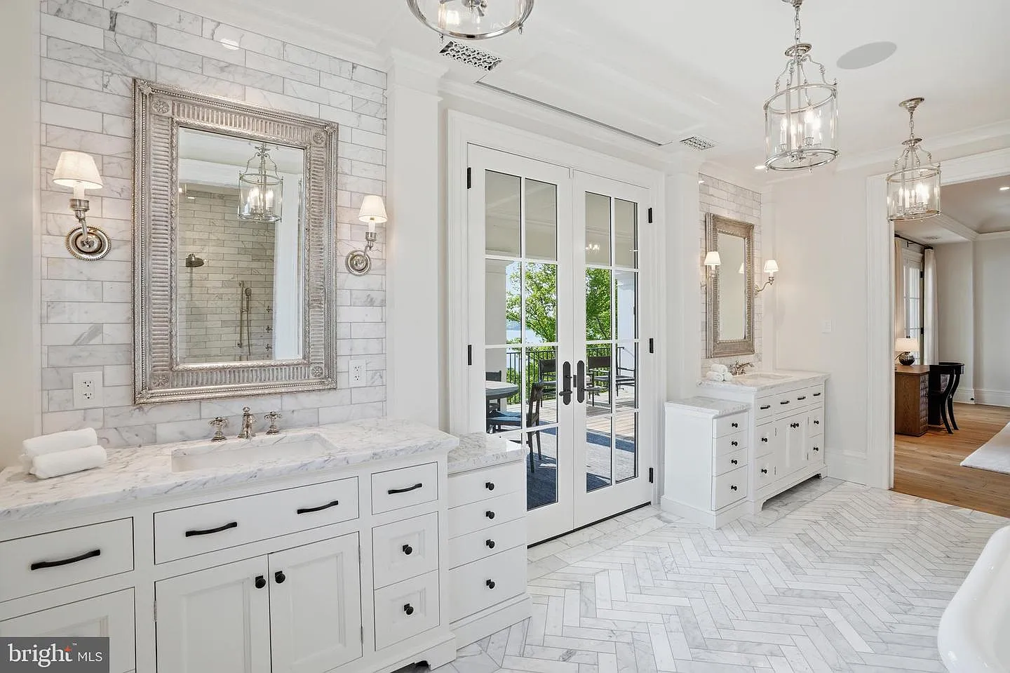 The suite flows directly into a marble bathroom with dual vanities that stretch beneath oversized framed mirrors and decorative lantern lighting.