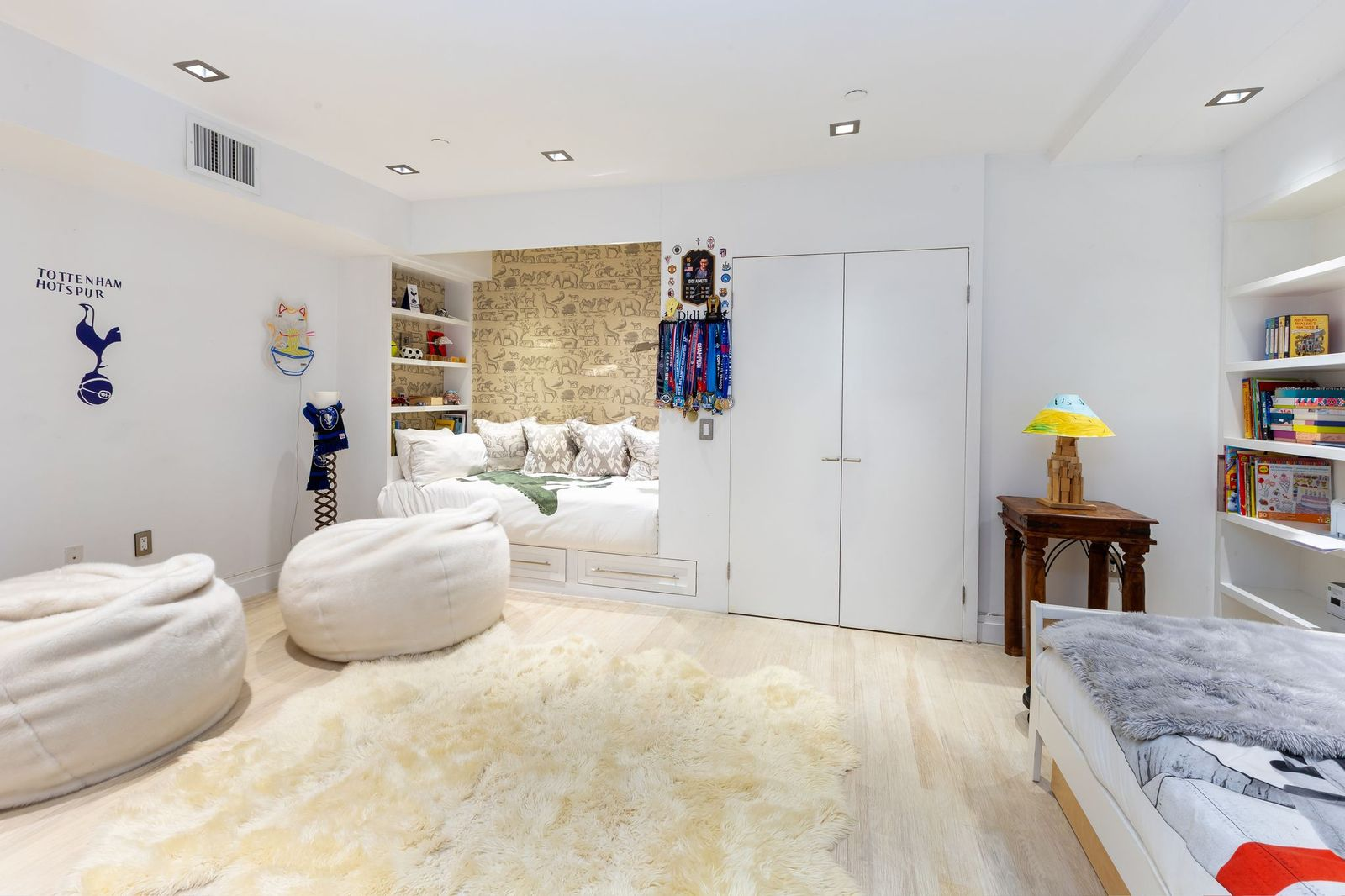 The second lower-level bedroom has been designed as a kid's room for two, with a built-in sleeping nook framed by patterned wallpaper and another bed placed on the opposite side of the room.