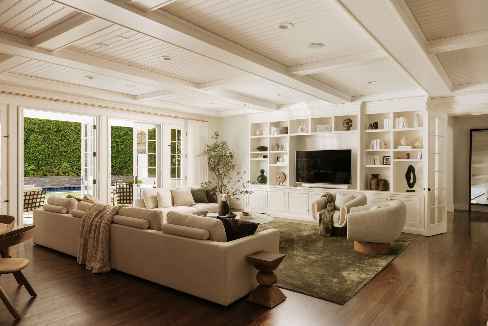 A coffered ceiling adds architectural detail overhead, while custom built-ins stretch across one wall, framing the television and providing display and storage space.