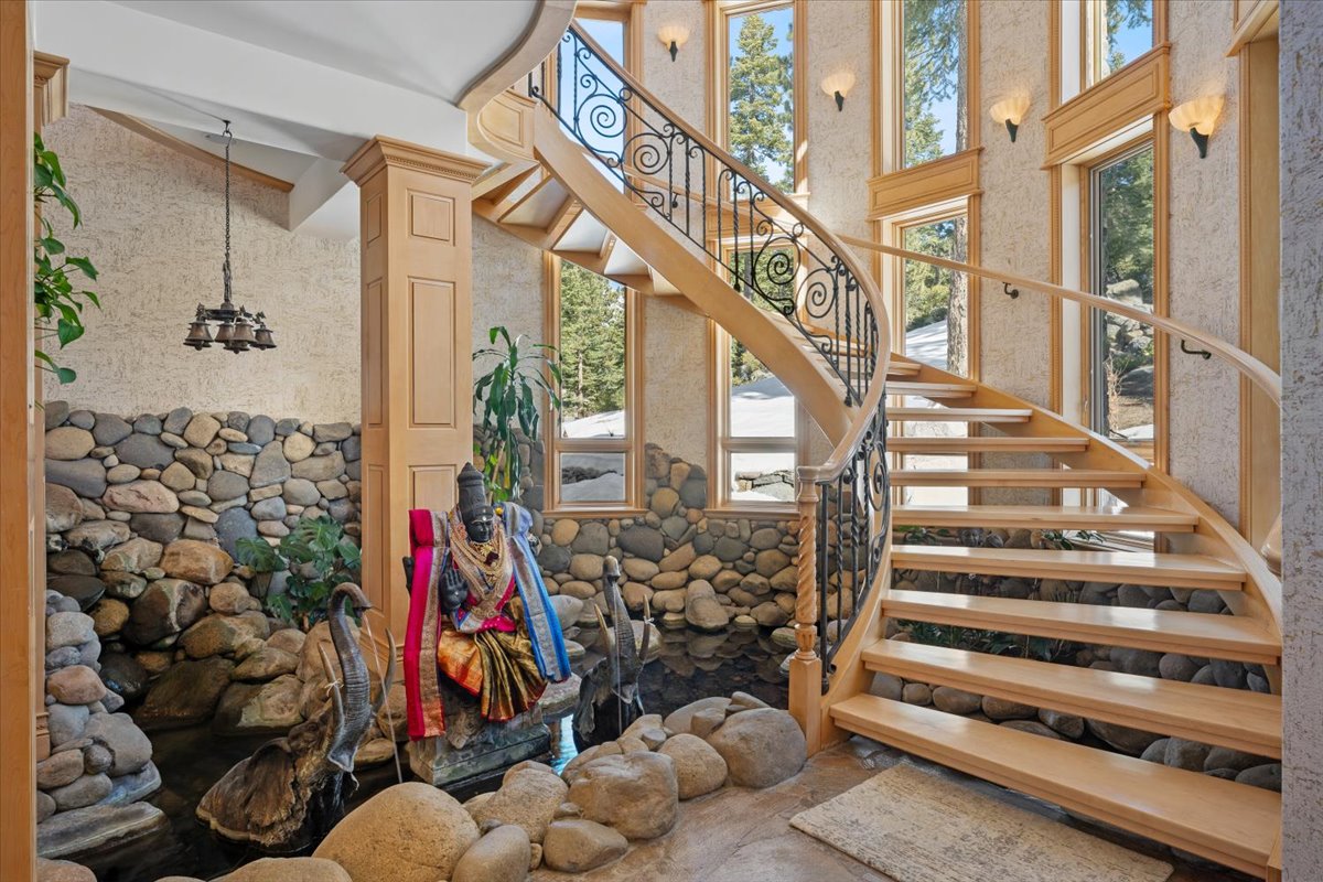 Slate floors lead into a soaring foyer with an indoor koi pond surrounded by river rock, draped statuary, and cobblestone wall accents,