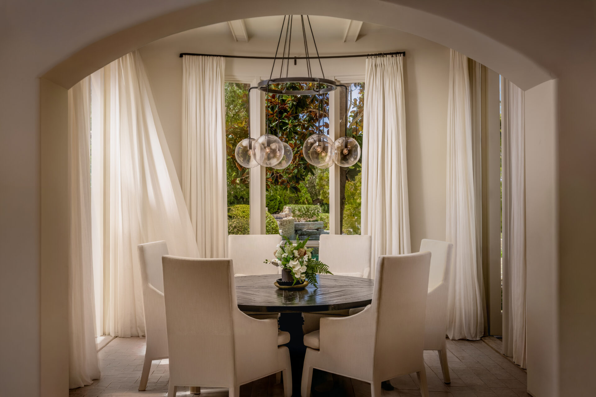 The breakfast nook is tucked beneath a wide arched opening and arranged around a round wood table with six upholstered chairs.