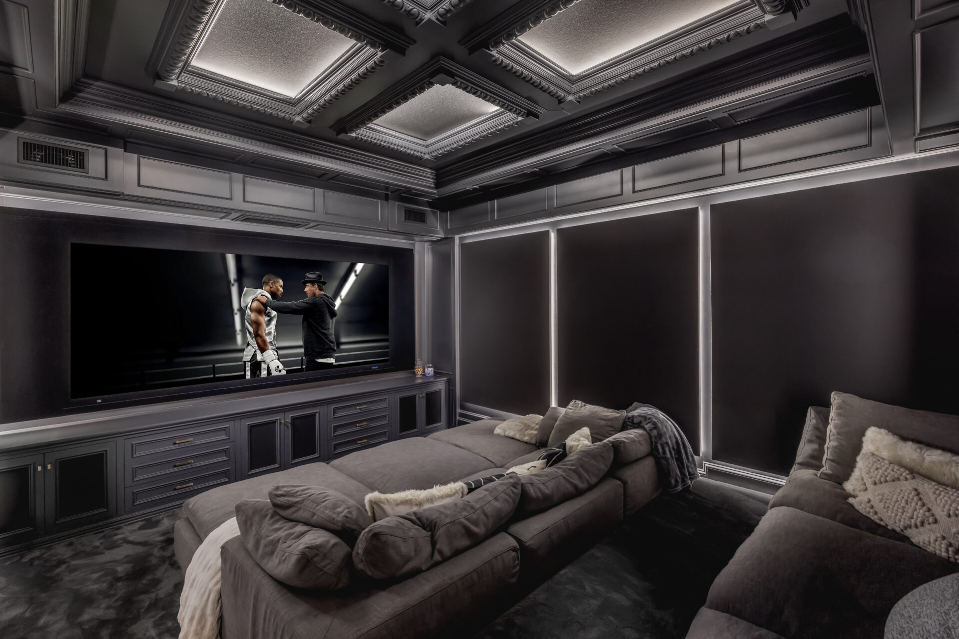 Deep sectional seating fills the center of the room facing a large built-in screen, while lower cabinetry stretches beneath it to create a clean, integrated media wall.