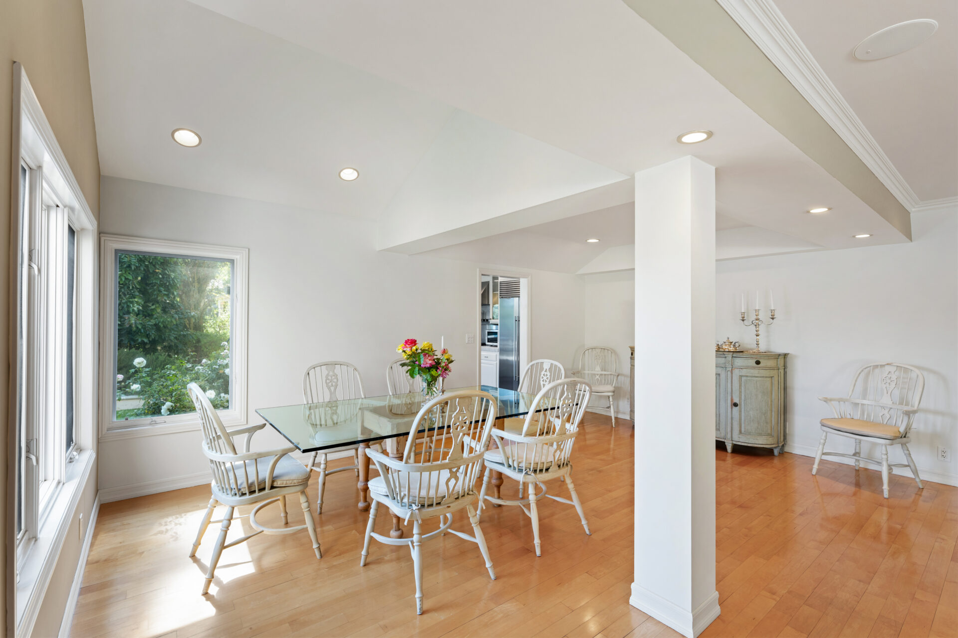 A glass-top dining table surrounded by white spindle-back chairs