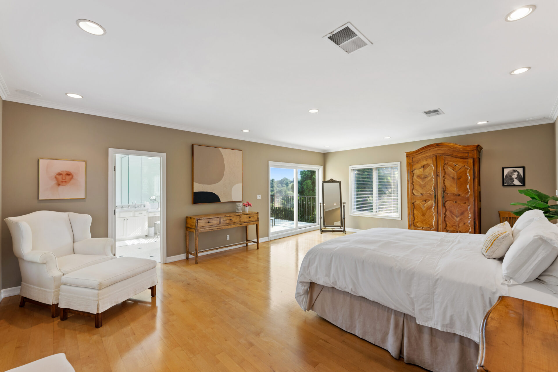 The primary suite sits in a corner of the upper level, with light hardwood floors, light brown walls, and enough room for a sitting area in addition to the bed. 