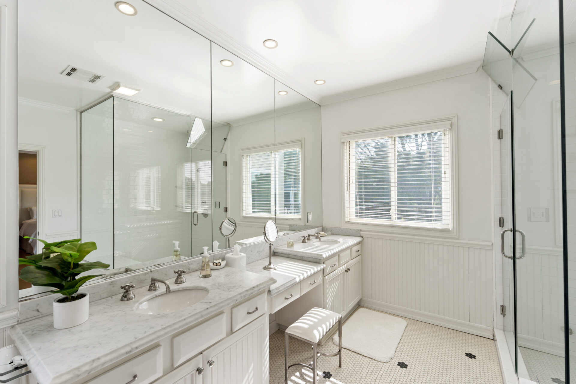 Bathroom with marble countertops, dual vanities, beadboard cabinetry, and oversized mirrors.