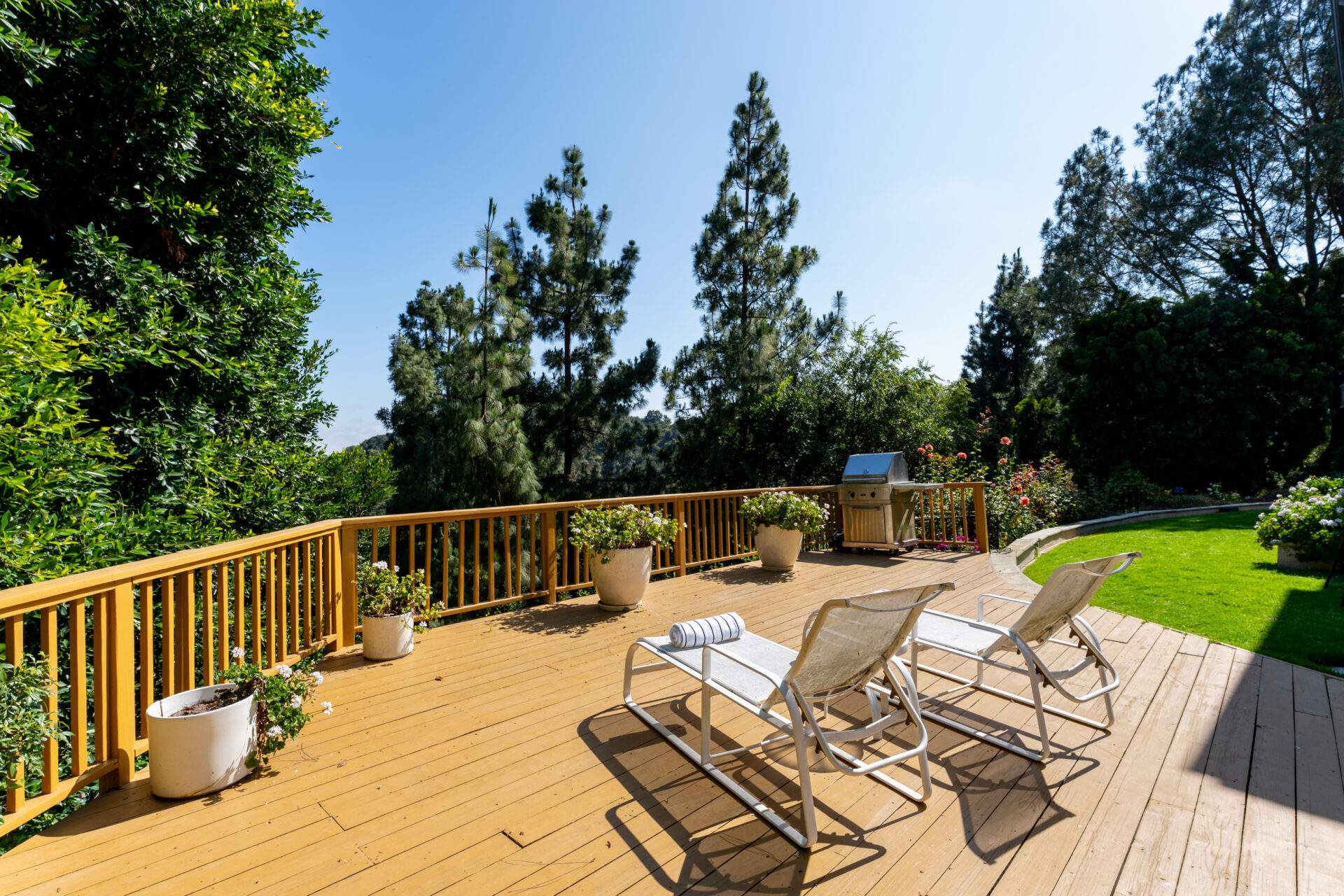 A large wood patio overlooks the canyon and includes space for lounge chairs, a grill, and potted plants along the railing.