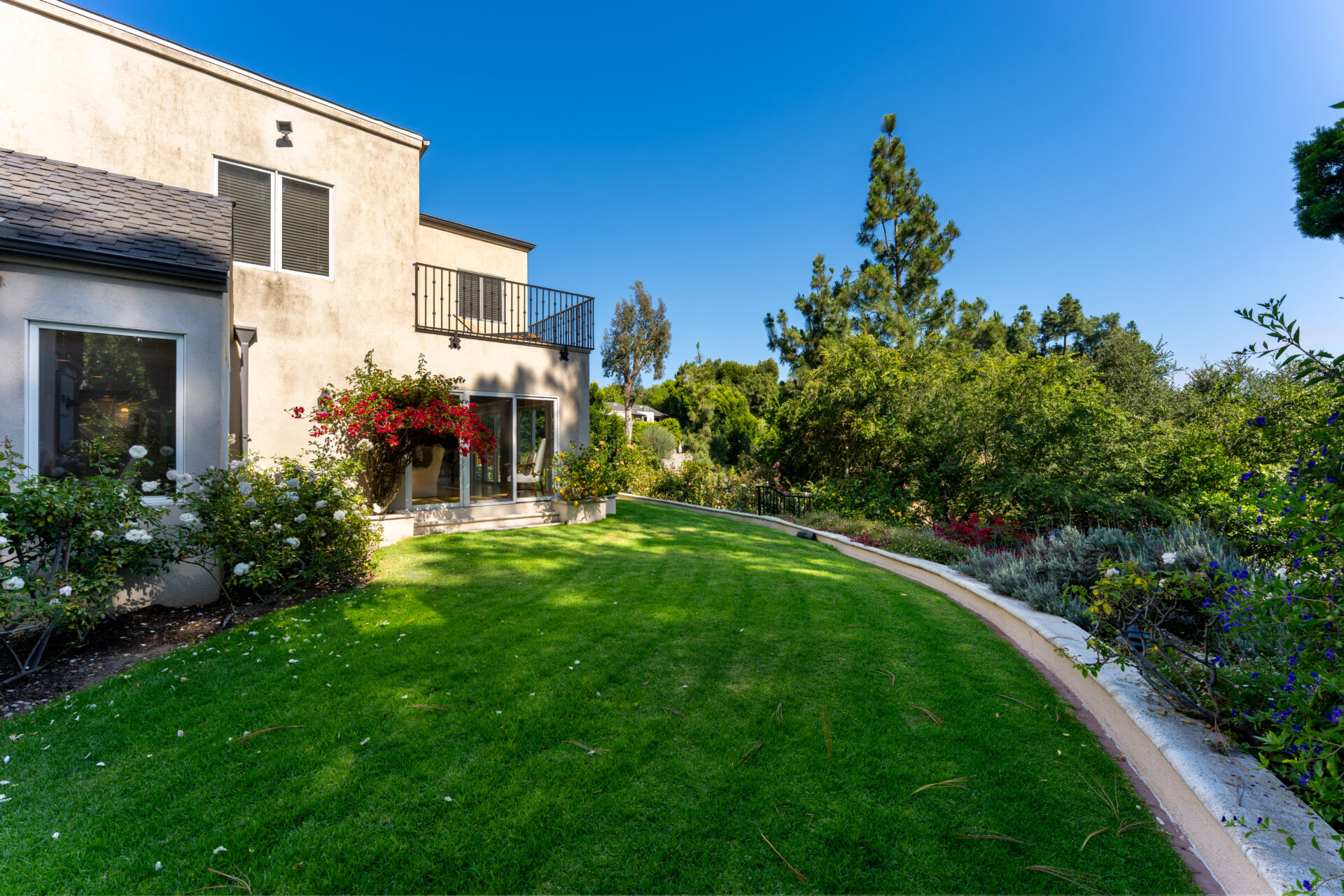 A broad lawn that wraps around the side of the home, creating an open grassy area bordered by colorful landscaping.