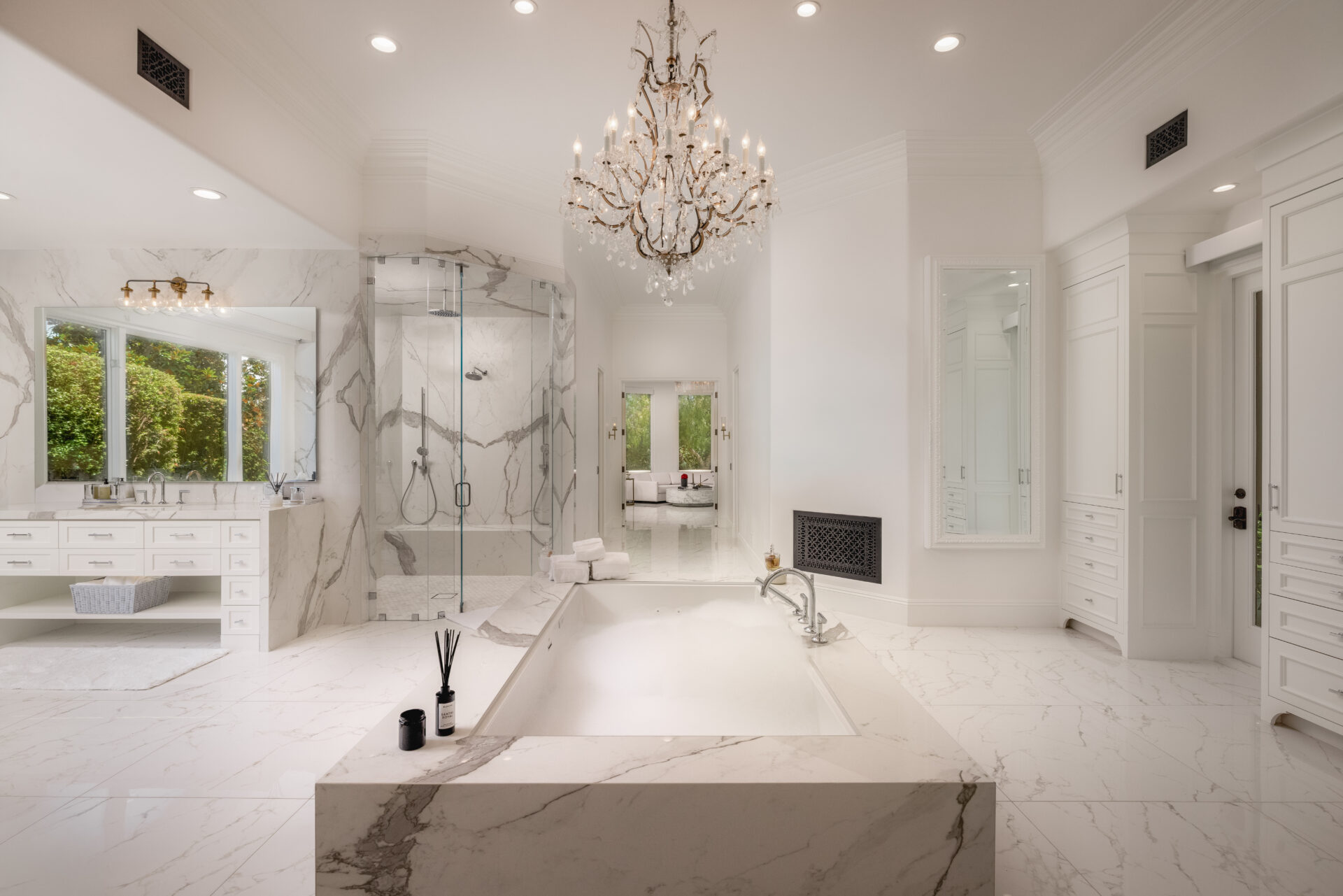 In the bathroom, the suite shifts into an all-white design finished in veined marble across the floors, tub surround, counters, and glass-enclosed shower.