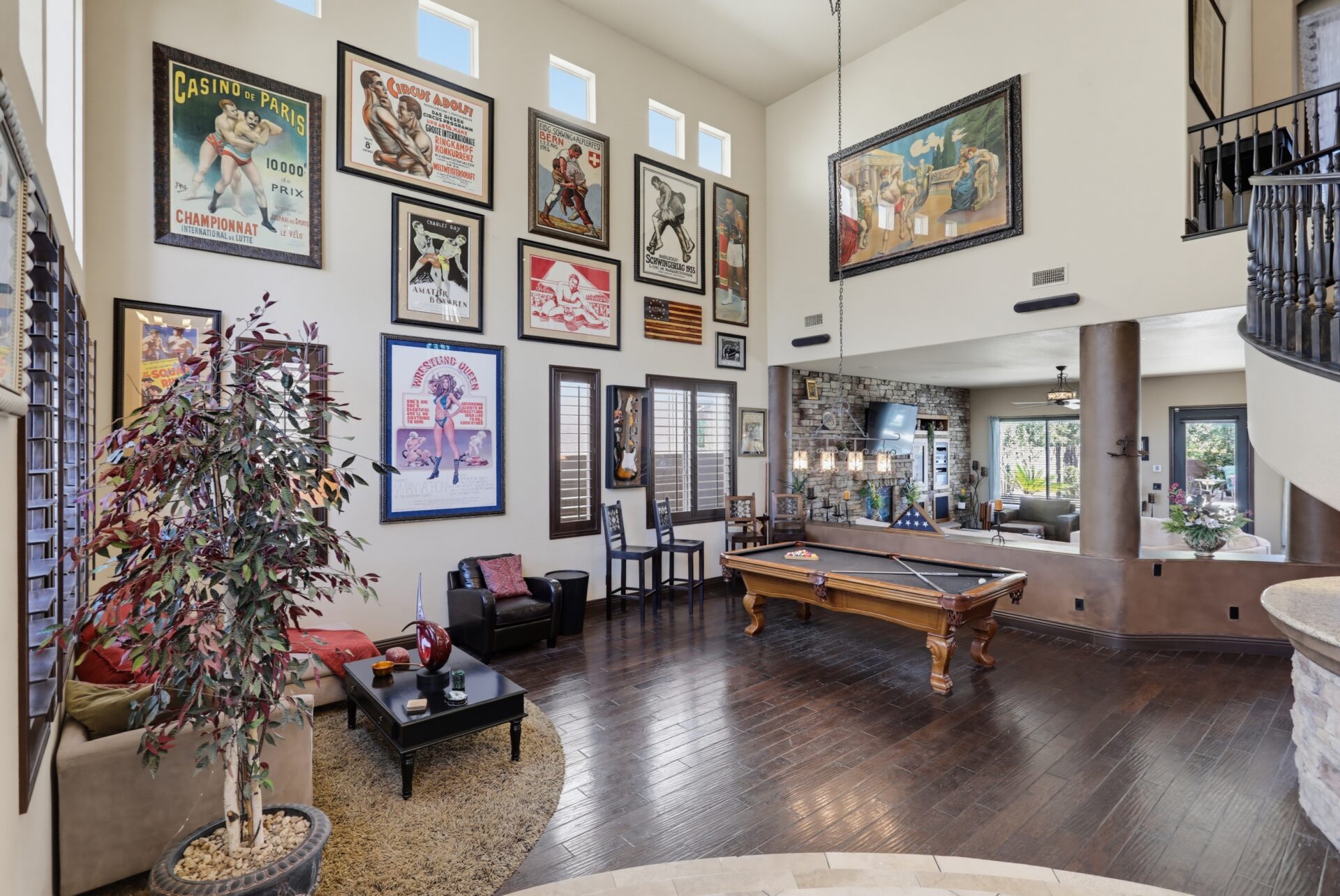 An expansive entertainment room centered around a billiards table, while a towering wall is lined with framed vintage wrestling posters. 
