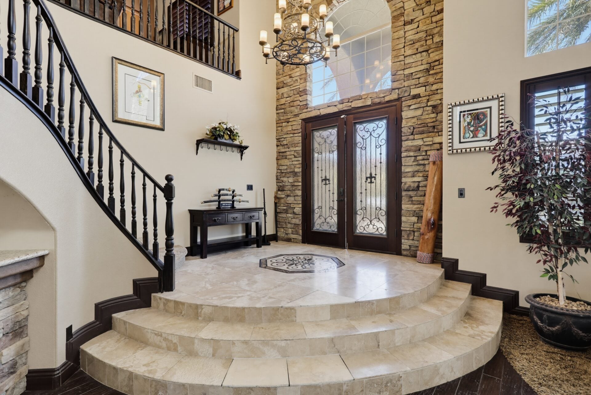 A two-story foyer where a curved staircase, stacked-stone accent wall, and wrought-iron double doors create a grand entry. 