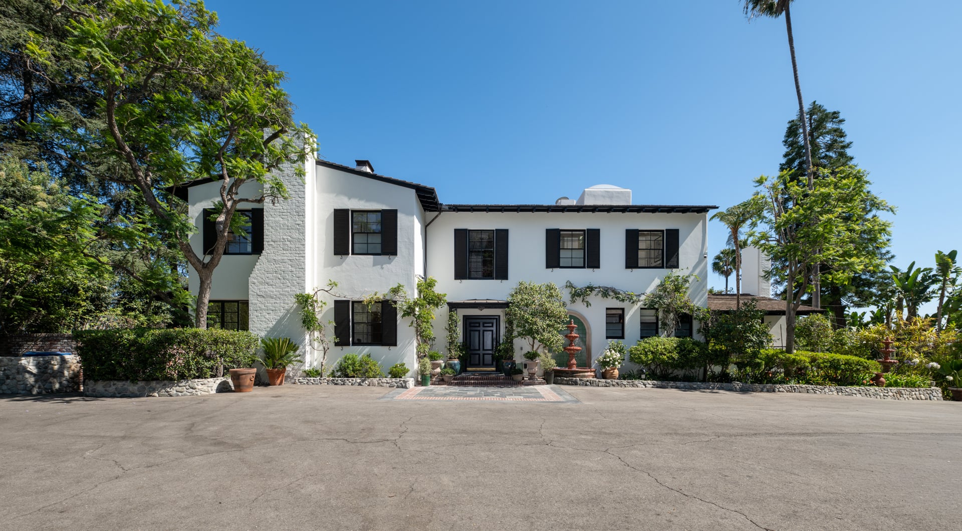 The drive opens to a broad motor court in front of the white stucco residence.