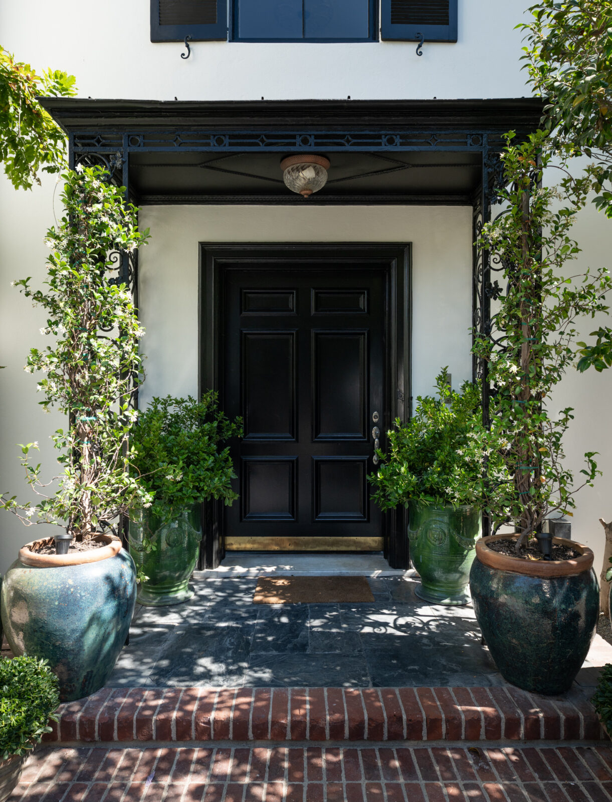 The home's vine-framed entrance past a couple of brick steps is framed by oversized planters, creating a welcoming arrival.