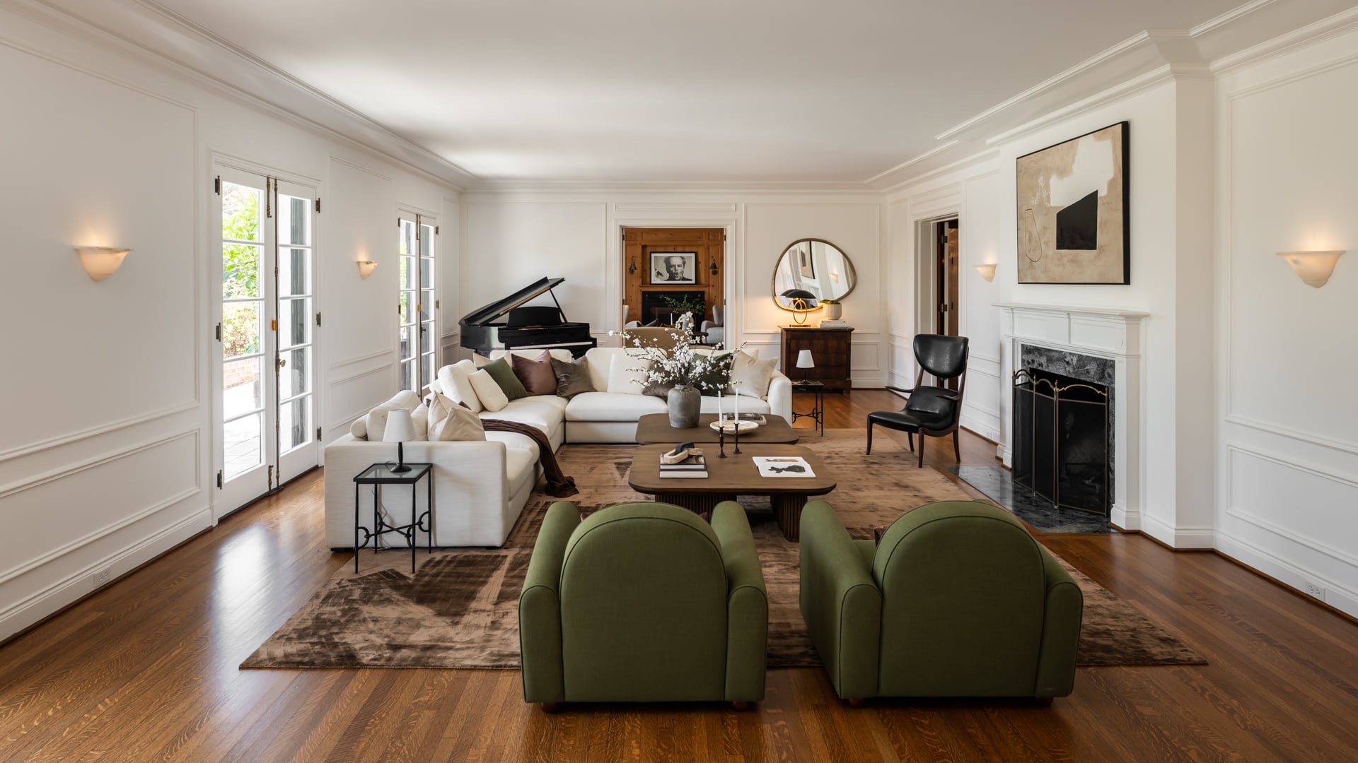 Between the fireplace and French doors, an L-shaped white couch, green armchairs, and a grand piano fill out the rest of the room.