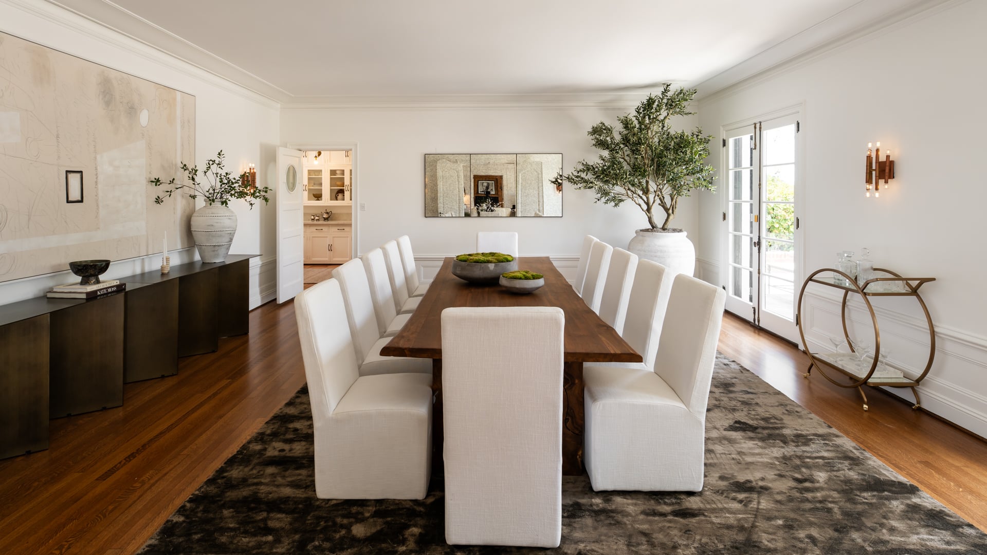 In the center, a long wood dining table is surrounded by white chairs offering room for a party of twelve.