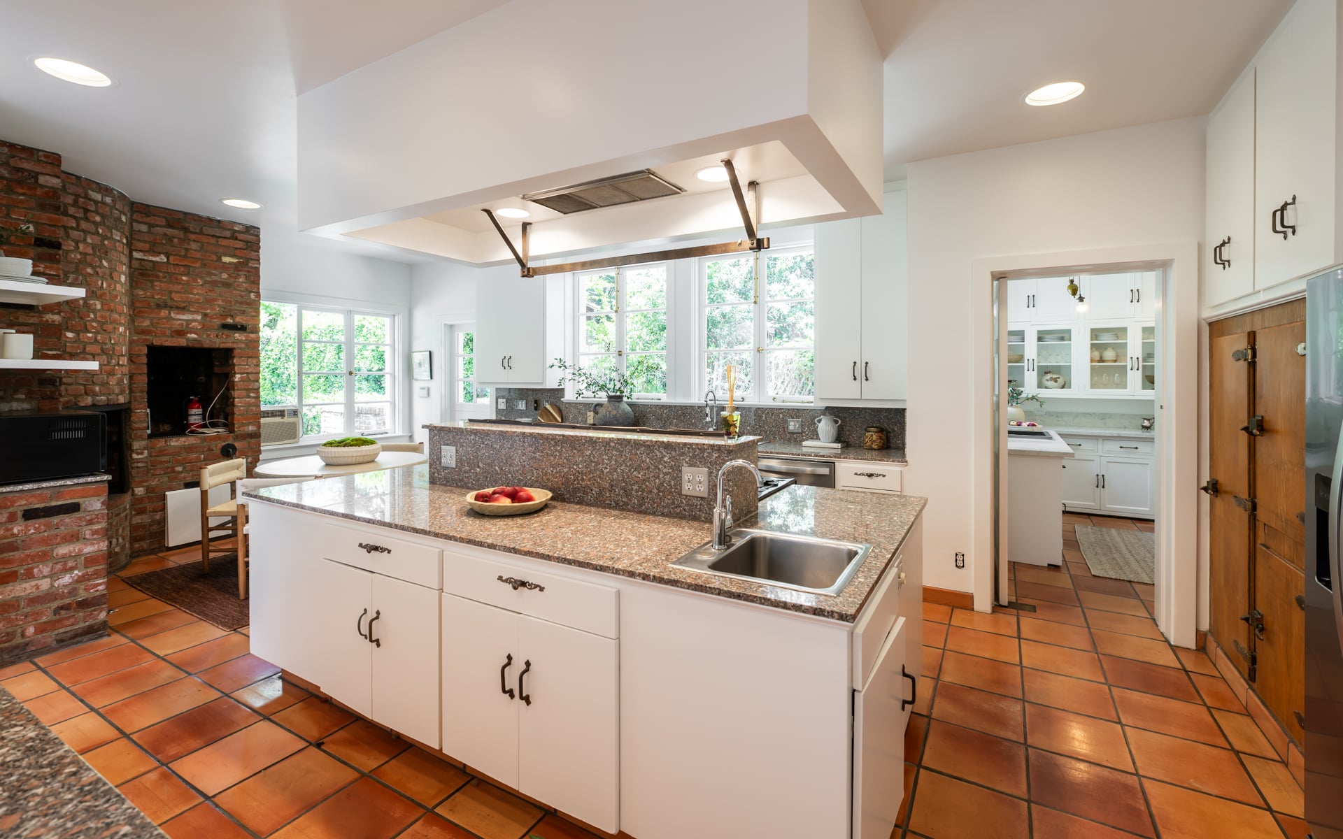 Kitchen with white cabinetry and granite countertops are paired with terracotta tile floors, while a large center island is home to the professional-style range.