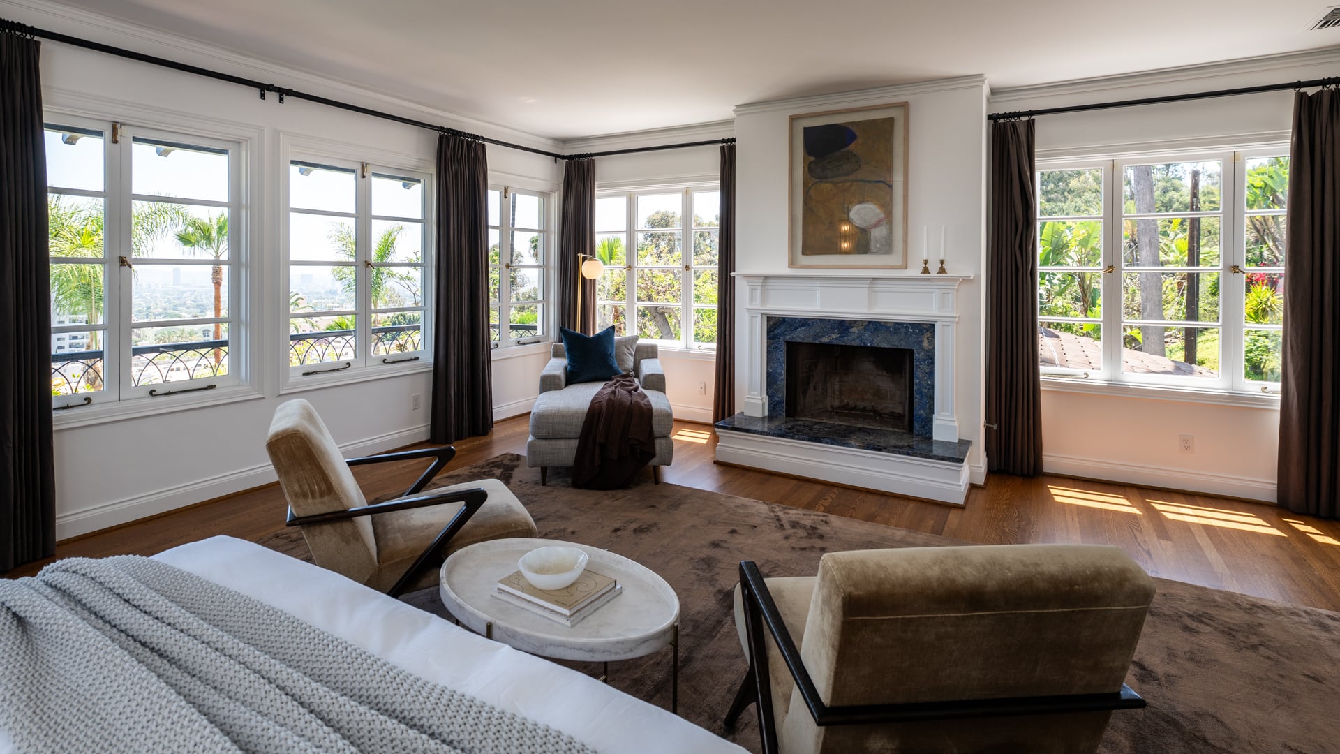 Inside, the bedroom is arranged around a fireplace framed by windows that fill the walls and are draped with black curtains.