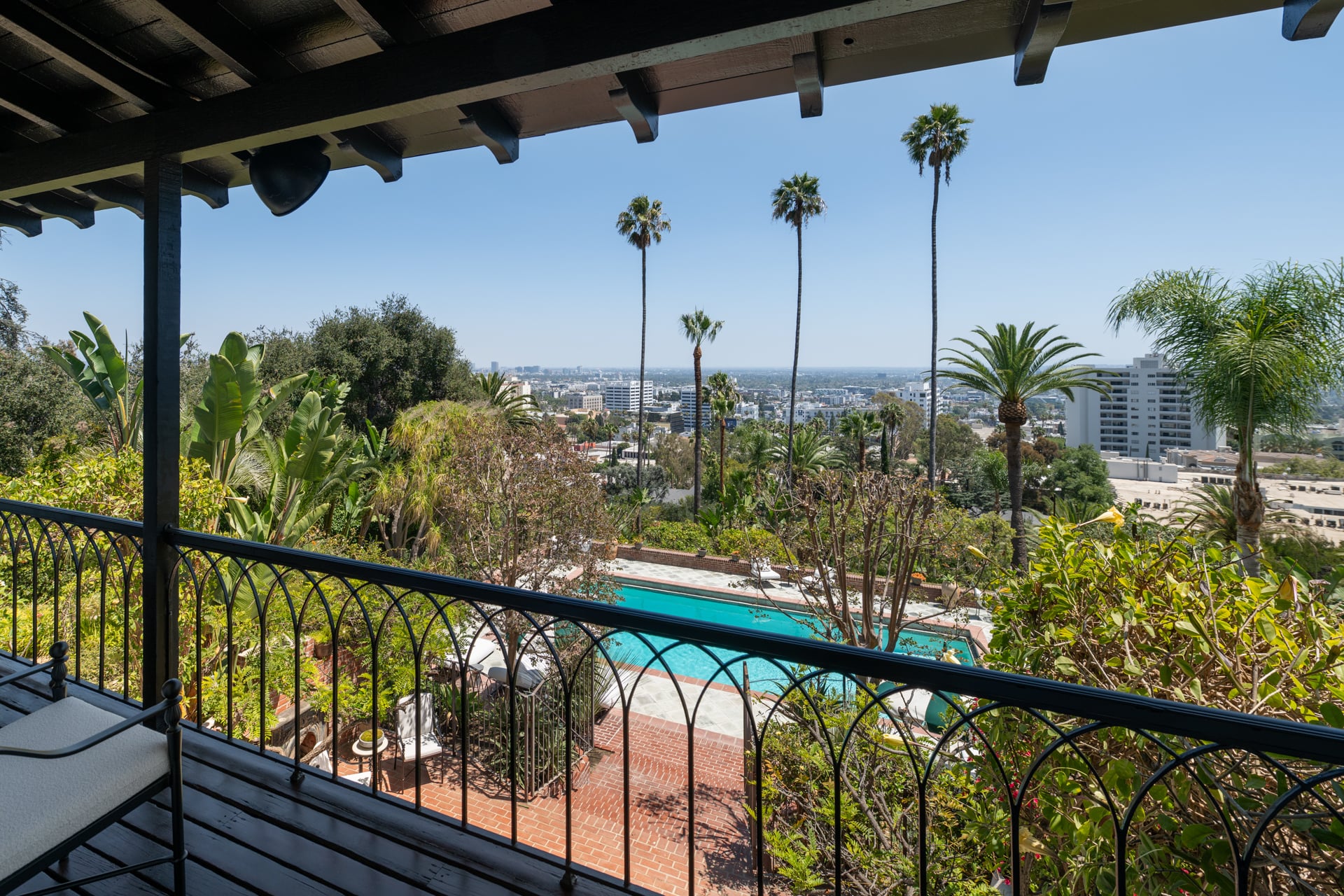 The covered balcony overlooks the pool, gardens, and palm-filled grounds before extending across the Los Angeles skyline. 